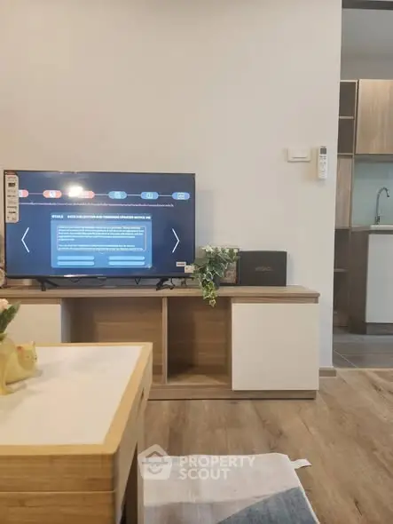Modern living room with stylish TV stand and open kitchen layout, featuring sleek wooden flooring.