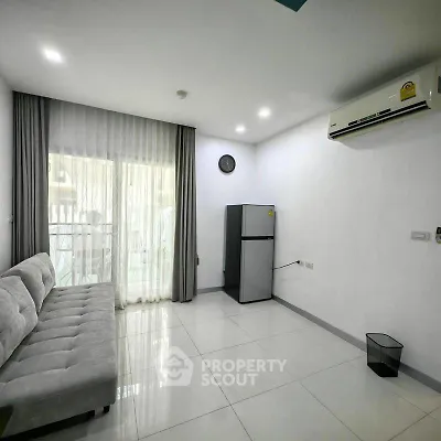 Modern living room with sleek sofa, air conditioning, and fridge, featuring large windows for natural light.