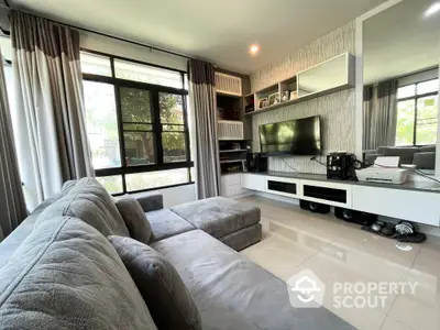 Spacious living room with large windows, plush sofa, and modern entertainment unit, bathed in natural light.