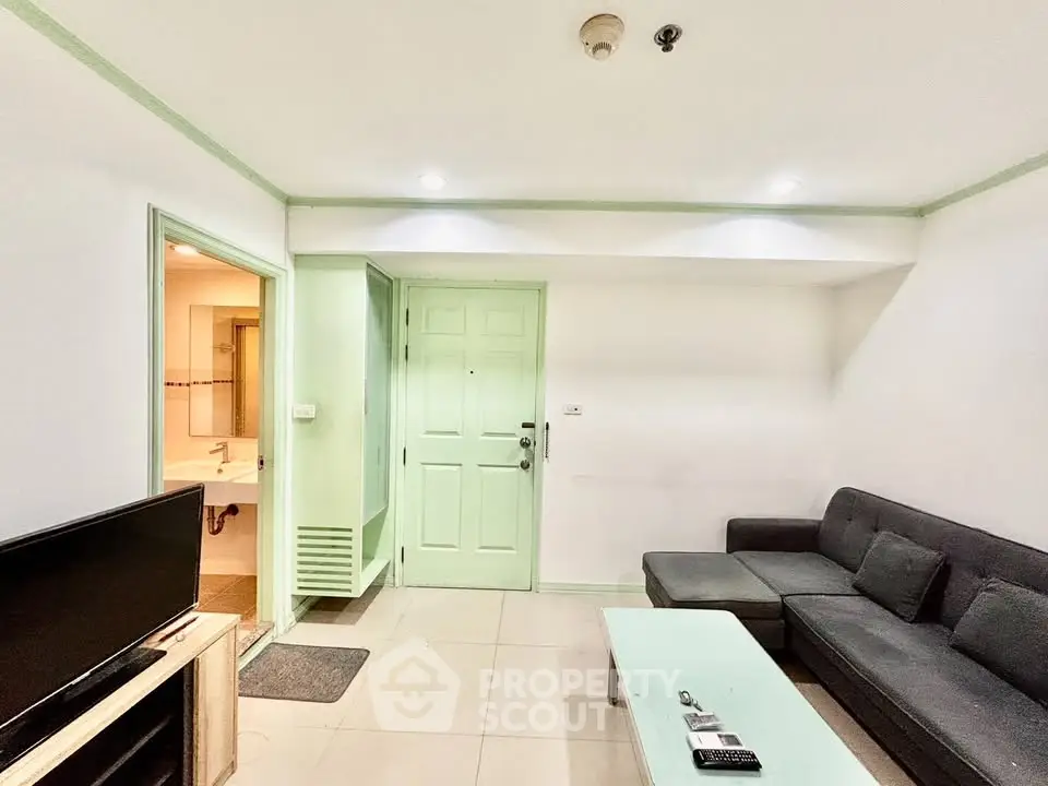 Cozy living room with modern sofa and TV, adjacent to a bathroom, featuring a mint green door and accents.