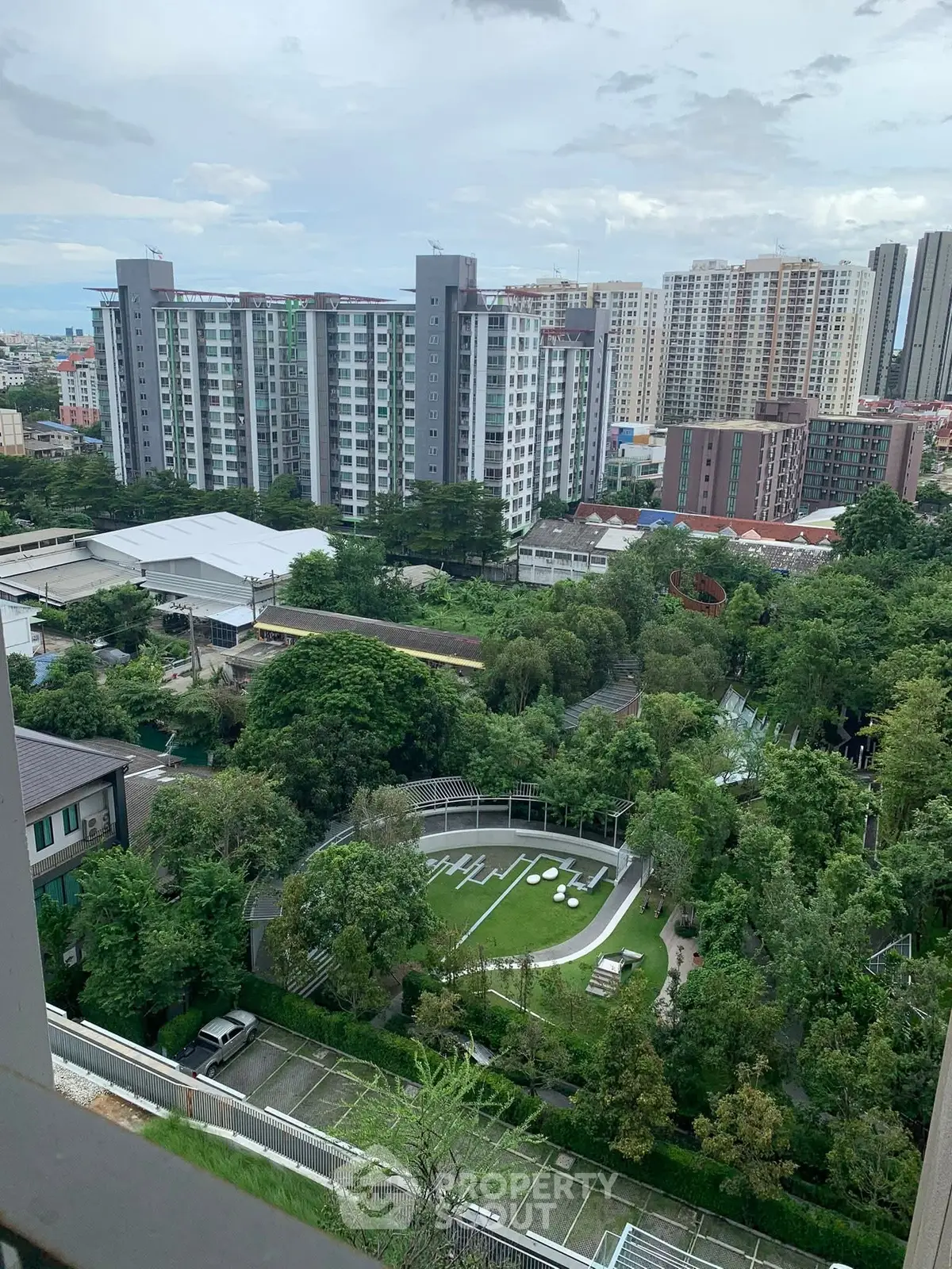 Stunning cityscape view from high-rise balcony overlooking lush gardens and modern buildings.