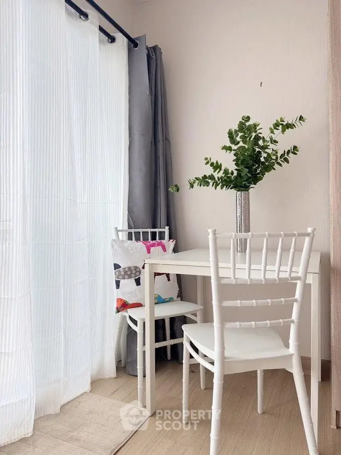 Cozy corner dining area with white chairs and table, accented by a vase of greenery, perfect for intimate meals.