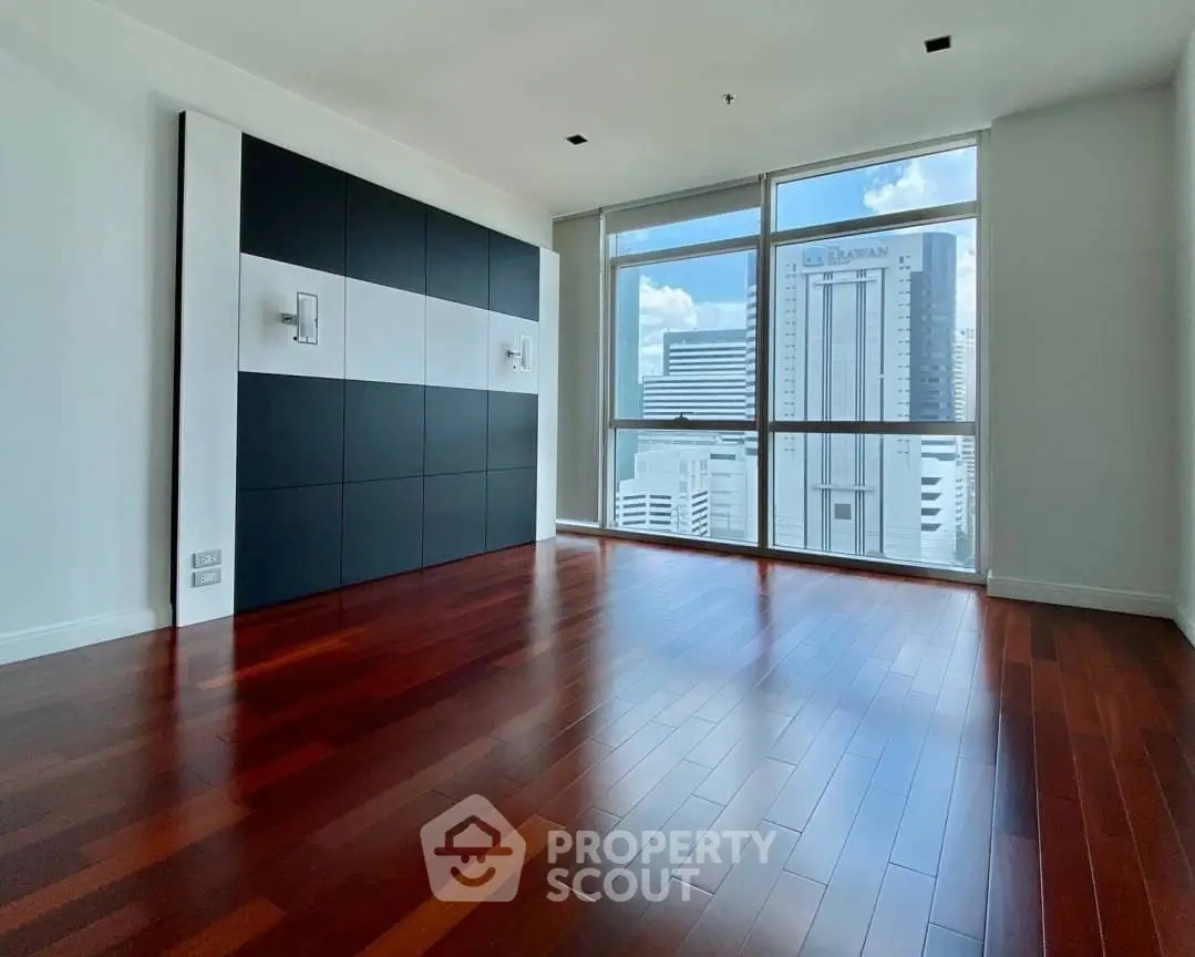 Spacious room with hardwood floors and city view through large windows.