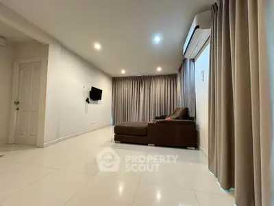 Spacious living room with modern sofa and wall-mounted TV, featuring elegant curtains and air conditioning.