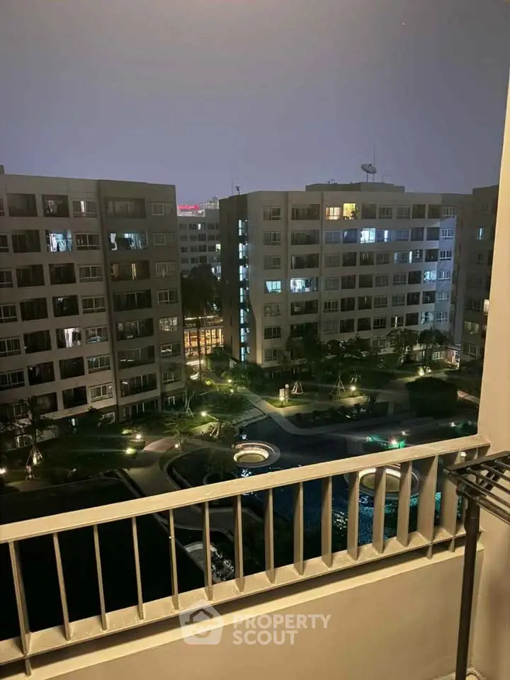 Night view from balcony overlooking illuminated apartment complex and pool area.