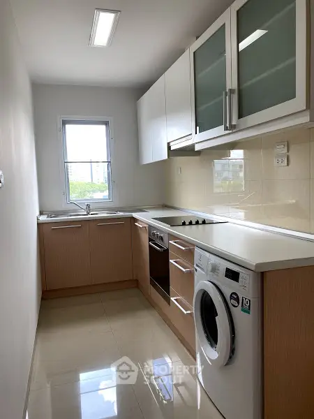 Modern kitchen with sleek cabinets, built-in oven, and washing machine under bright lighting.