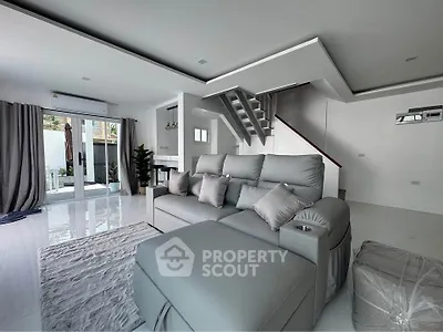 Spacious modern living room with sleek gray sofa and stylish staircase in a bright open layout.