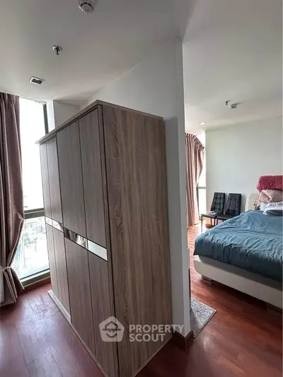 Spacious bedroom with wooden flooring and large windows offering natural light.