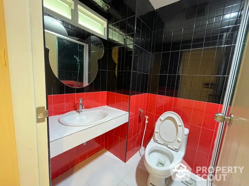 Modern bathroom with striking red and black tiles, featuring a sleek sink and toilet.