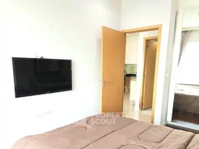 Modern bedroom with wall-mounted TV and open door leading to a bright hallway.