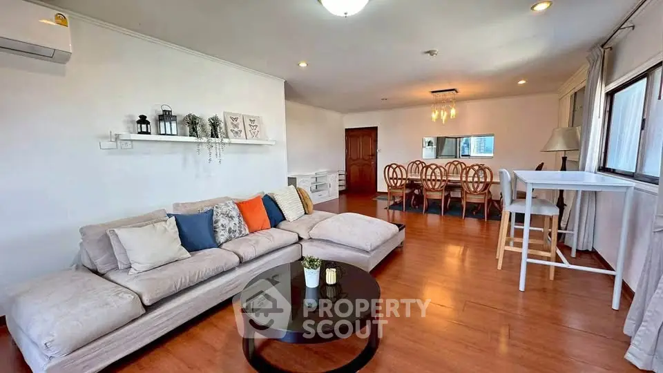 Spacious living room with modern decor and dining area, featuring wooden flooring and ample natural light.
