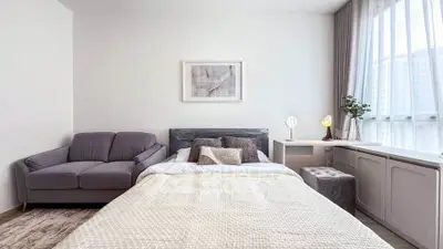 Modern bedroom with cozy bed, stylish sofa, and natural light from large window.