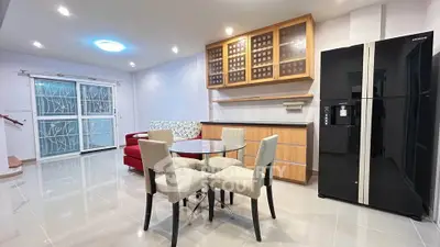 Modern open-plan living room with sleek kitchen and dining area, featuring stylish furniture and large refrigerator.