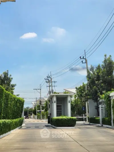 Charming gated community entrance with lush greenery and clear blue sky.