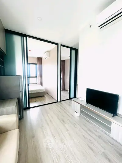 Modern living room with sleek design, featuring a TV and air conditioning, leading to a cozy bedroom.