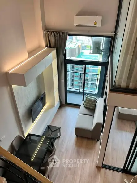 Modern loft-style living room with high ceiling and large windows offering city views.