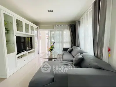 Spacious living room with modern gray sofa and large TV unit, flooded with natural light.