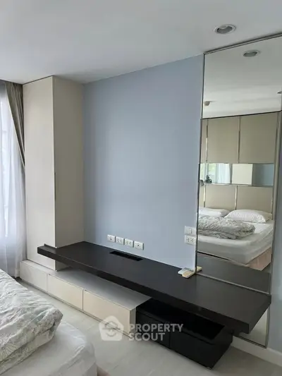 Modern bedroom with sleek built-in furniture and large mirror, enhancing space and light.