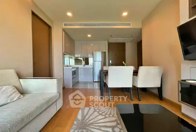 Modern living room with open kitchen and dining area, featuring sleek furniture and wooden flooring.