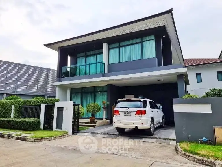 Modern two-story house with driveway and parked SUV, featuring sleek design and lush landscaping.