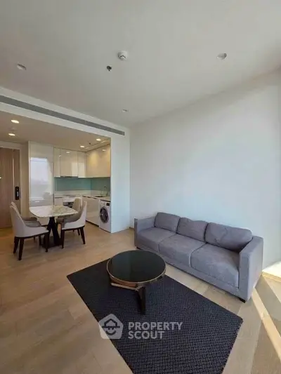 Modern living room with open kitchen, featuring sleek furniture and natural light.