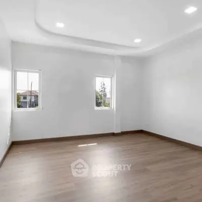 Spacious empty room with wooden flooring and natural light from two windows.