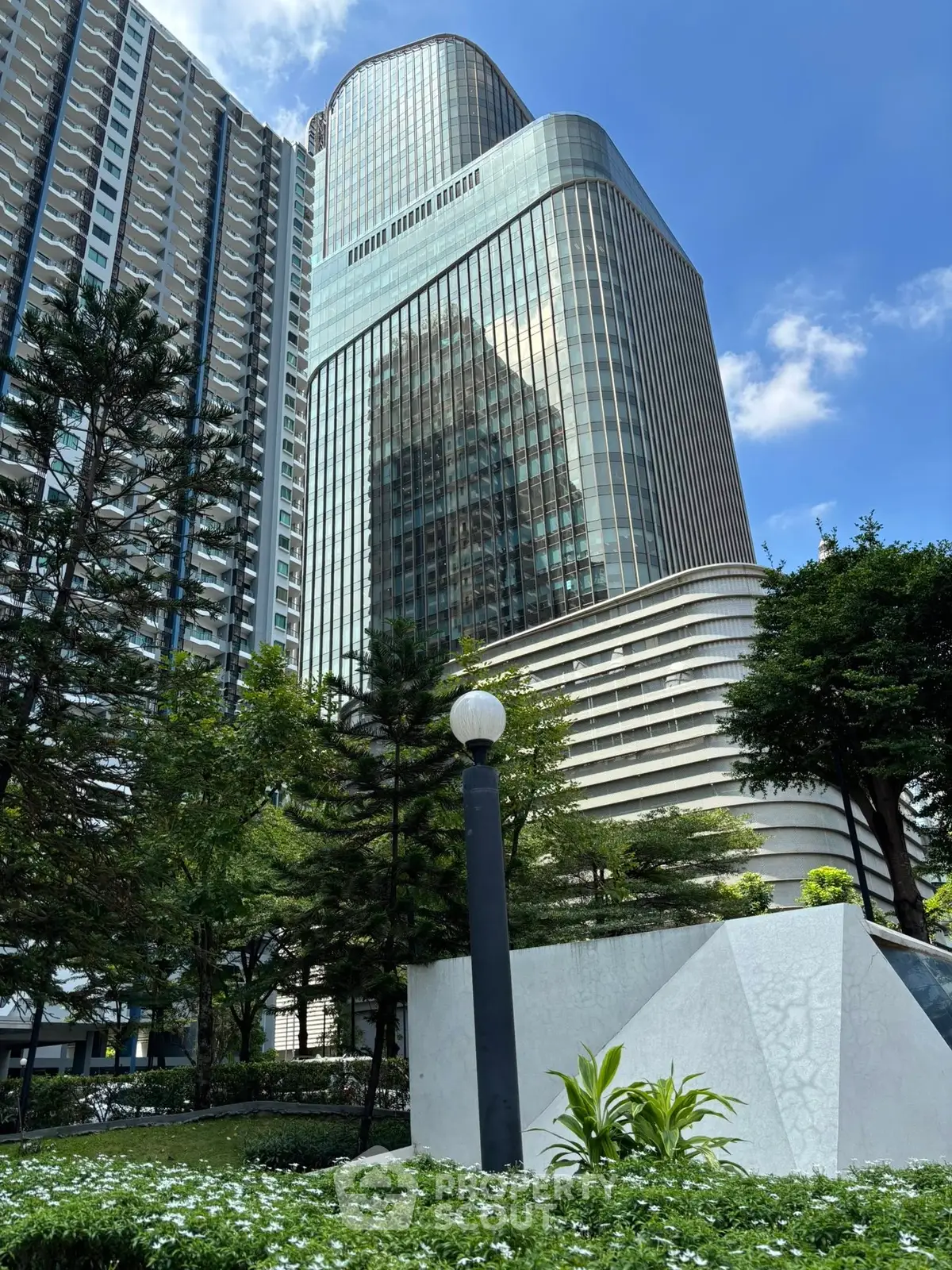 Stunning modern skyscraper with lush green landscaping and clear blue sky.