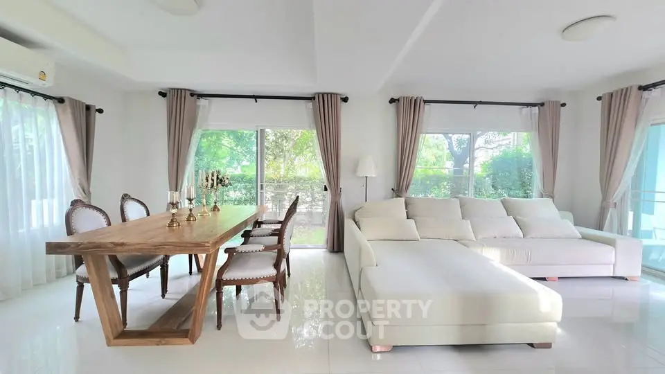 Spacious living room with elegant dining area and large windows offering garden views.
