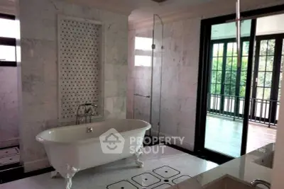 Luxurious bathroom with elegant freestanding bathtub and large windows overlooking balcony.
