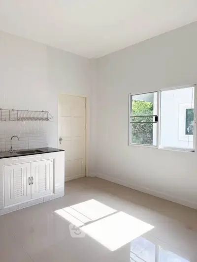 Bright minimalist kitchen with white cabinetry and large window, perfect for modern living.