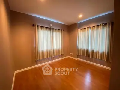 Spacious empty room with wooden flooring and elegant curtains, perfect for customization.