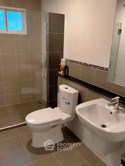 Modern bathroom with sleek fixtures and neutral tiles, featuring a shower and toilet.