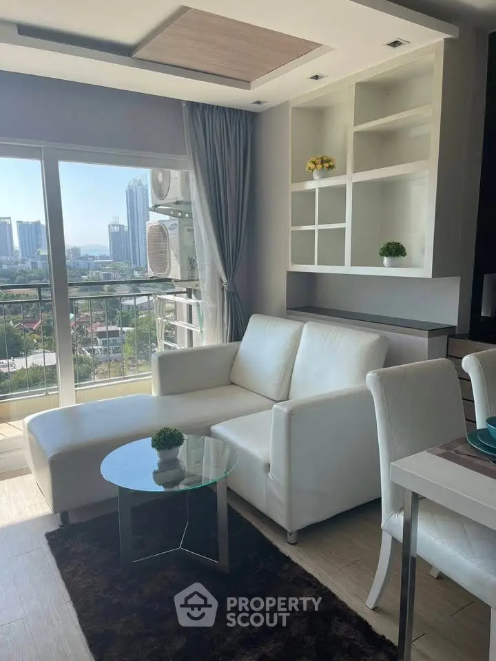 Modern living room with white sofa, glass table, and city view from balcony in high-rise apartment.