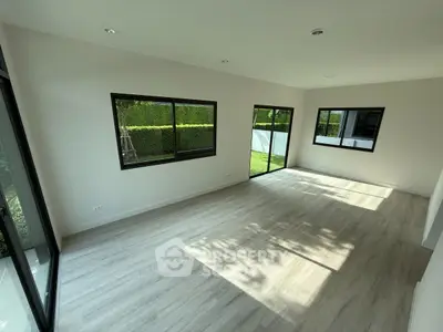 Spacious sunlit room with large windows and modern flooring, ideal for versatile living space.