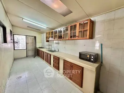 Spacious kitchen with wooden cabinets and tiled flooring, featuring a microwave and ample counter space.