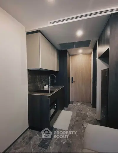 Modern compact kitchen with sleek cabinetry and stone flooring in a stylish apartment.