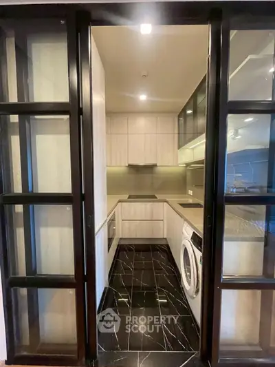 Modern kitchen with sleek cabinetry and built-in appliances, featuring a washing machine and elegant black flooring.