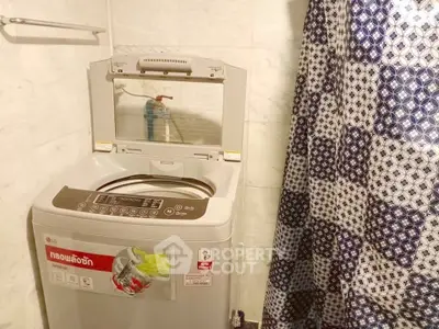 Compact bathroom with washing machine and patterned shower curtain.