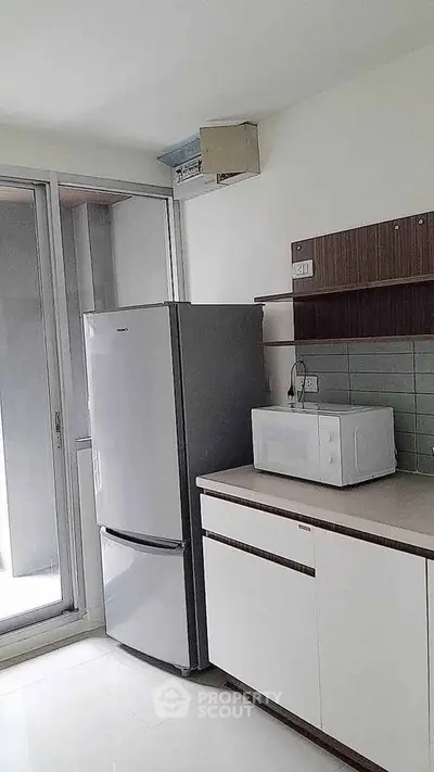 Modern kitchen with sleek cabinets, fridge, and microwave near large window.
