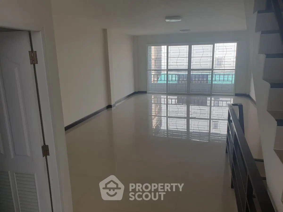 Spacious empty living room with large windows and staircase, perfect for customization.