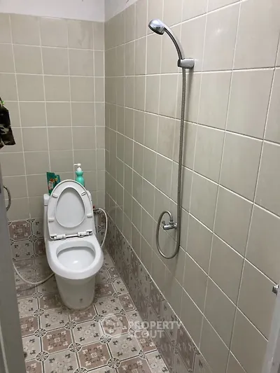 Compact bathroom with tiled walls and floor, featuring a toilet and shower setup.