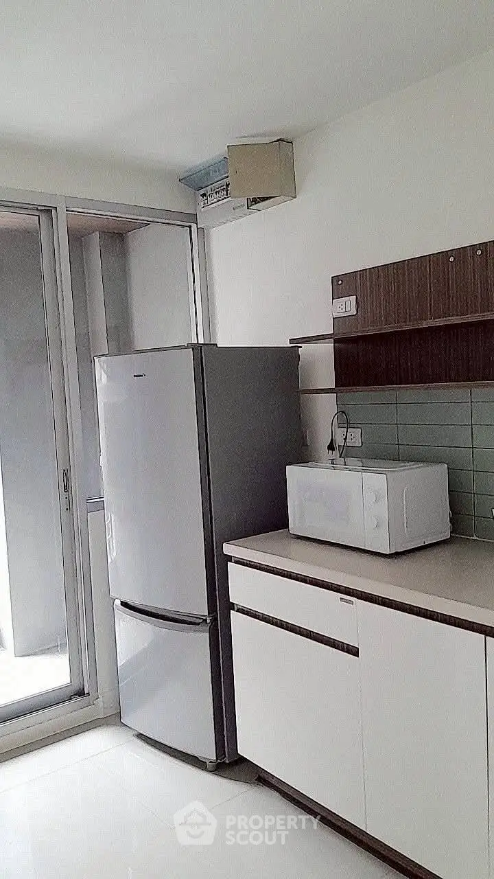 Modern kitchen with sleek fridge and microwave, featuring a minimalist design and ample natural light.