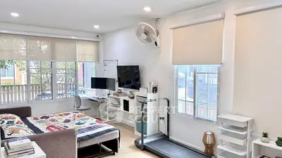 Spacious modern bedroom with treadmill and study area, featuring large windows and cozy decor.