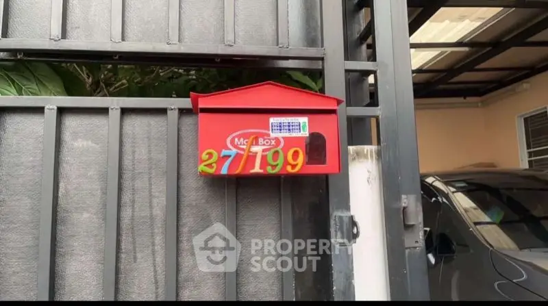 Charming red mailbox on a modern gate with carport in background.