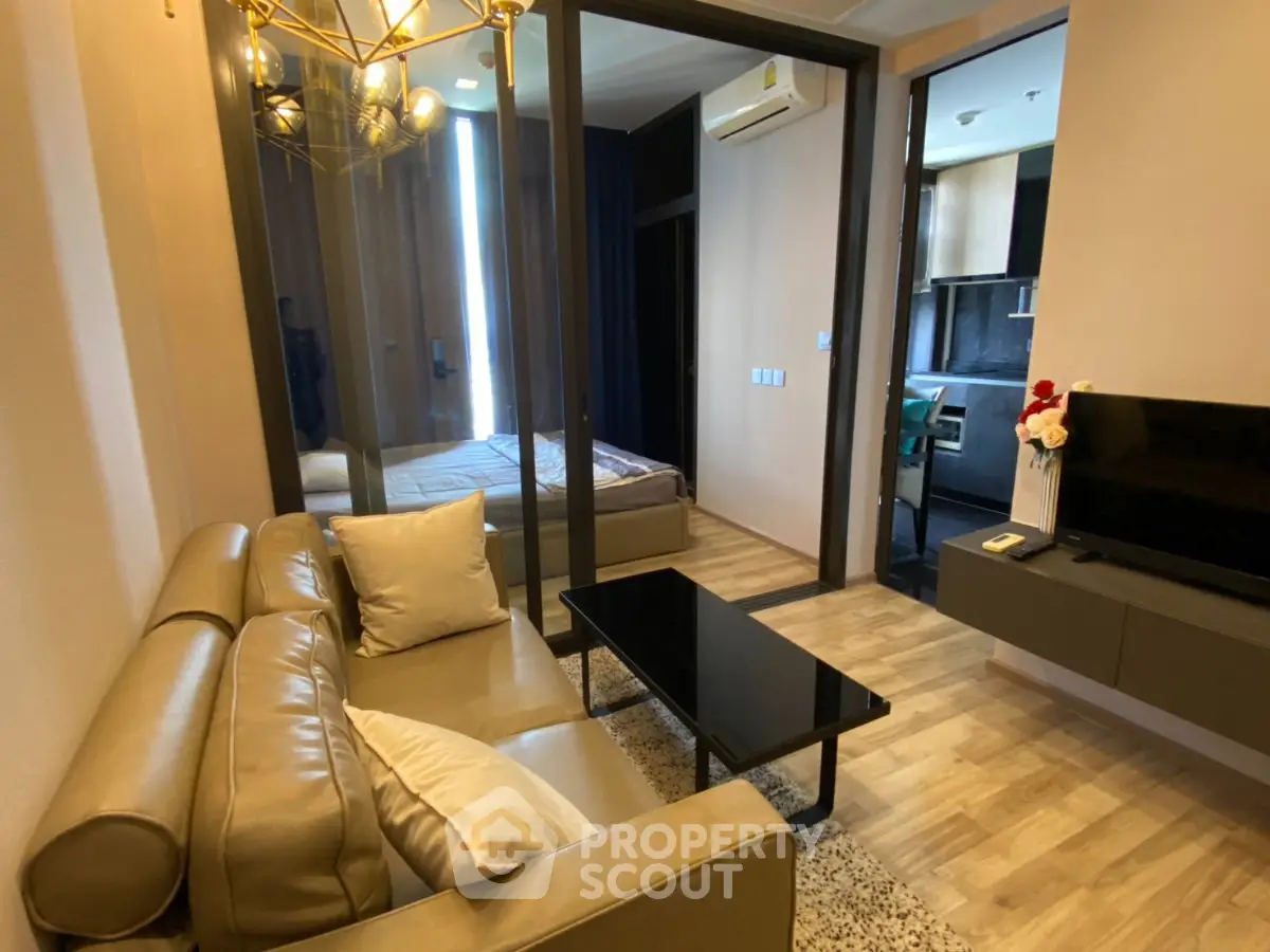 Modern living room with sleek furniture and open view into bedroom, featuring elegant decor and natural lighting.
