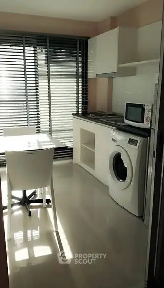 Modern kitchen with washing machine and dining area, featuring sleek design and ample natural light.