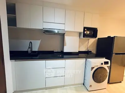 Modern kitchen with sleek cabinetry, washing machine, and black countertops.