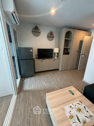 Modern living room with sleek wooden flooring, stylish TV unit, and compact refrigerator.