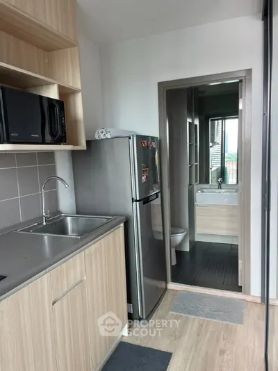 Modern compact kitchen with sleek appliances and adjacent bathroom view