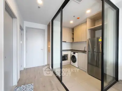 Modern kitchen with glass partition, stainless steel fridge, and washing machine in sleek apartment.